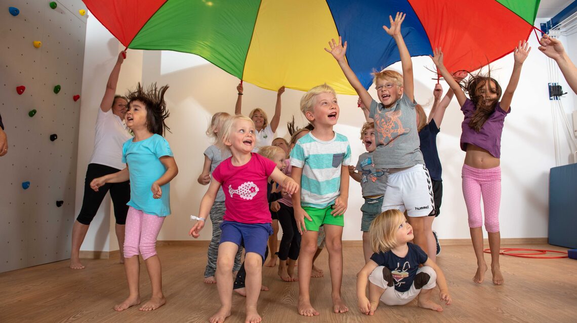 Kindergruppe springt jubelnd unter dem bunten Schwungtuch bei SportStart Winterhude